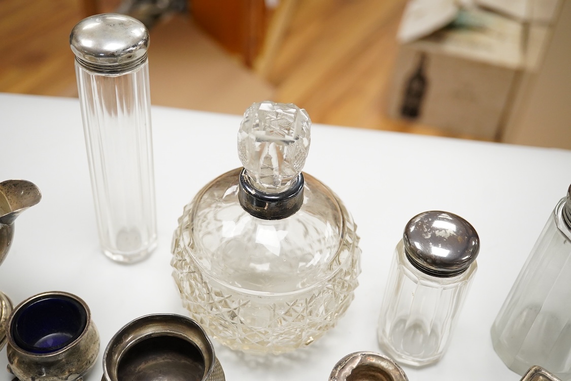 An early 20th century silver mounted cut glass scent bottle, five silver mounted glass toilet jars, a pair of silver mounted dwarf candlesticks, two silver condiments, a sterling jug(weighted), a sterling cup and cover(w